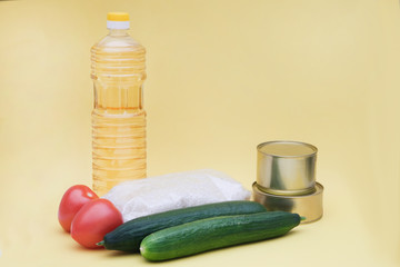 Crisis food stocks for the period of quarantine isolation on a yellow background. Rice, cucumbers, canned food, tomatoes, oil. Food delivery, coronavirus quarantine. Copyspace.
