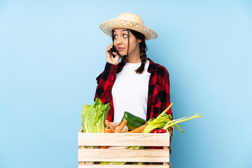 Young farmer Woman holding fresh vegetables in a wooden basket keeping a conversation with the mobile phone with someone