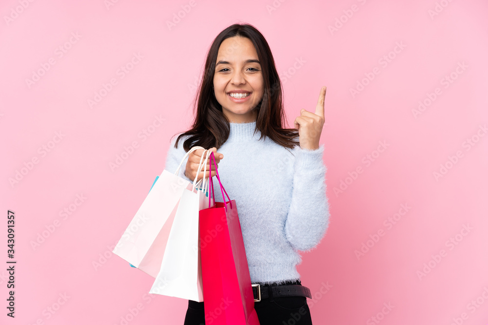 Wall mural Young woman with shopping bag over isolated pink background pointing up a great idea