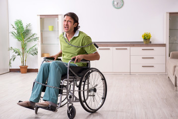 Young male invalid in wheel-chair suffering at home