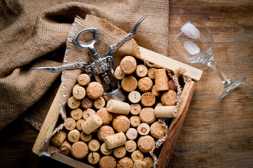 Wine corks of different sizes, a corkscrew, a bottle of wine and a glass shot on an old wooden surface. Background for liquor.