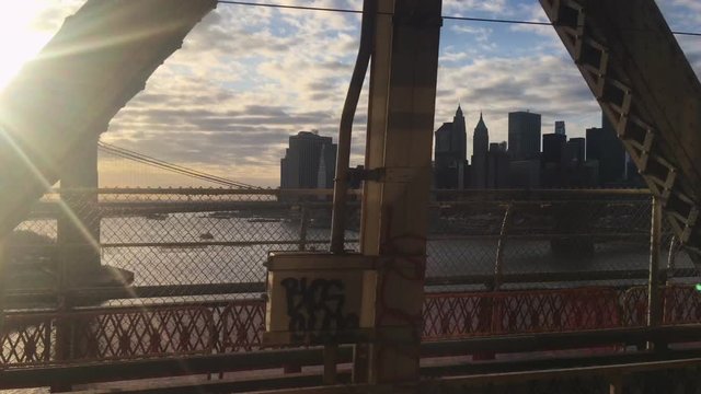 Glimpse of Manhattan and the Brooklyn Bridge at sunset interspersed with the passage of metal beams from the subway window while crossing the East River on a bridge in the direction of Downtown