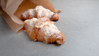 Freshly baked croissants in a package of craft paper on a grey tile background .
