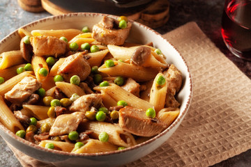 Homemade pasta with green peas, chicken and sauce on a dark background