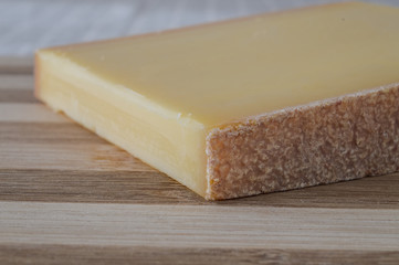 slice of french comte cheese on wood cutting board closeup