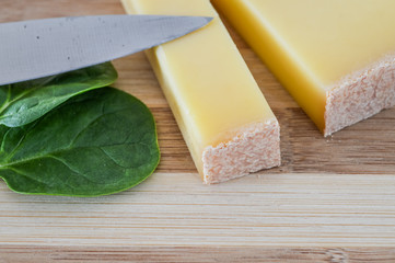 slice of french comte cheese on wood cutting board with fresh green spinach leaves closeup