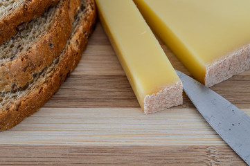 slice of french comte cheese on wood cutting board with fresh green spinach leaves and sliced 7-grain bread closeup