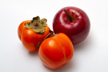 One red apple and two persimmons on a light background