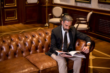 Mature man in elegant suit reading a book in a luxurious apartment