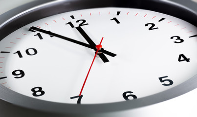 It is five to twelve, the clock is ticking. Modern white grey clock shows the time 5 before 12. Close up to a wall clock, with five minutes to twelve o'clock. Time is running out 