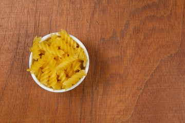 bowl with raw pasta on wooden background.