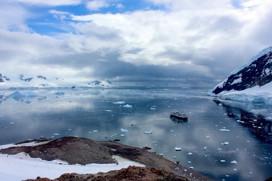 High Angle View Of Boat Moving On Lake Amidst Snow Covered Mountains Against Cloudy Sky