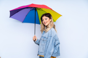 Teenager russian girl holding an umbrella isolated on blue background smiling a lot