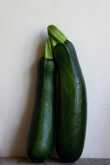 Two Green Zucchini Standing Near The White Wall