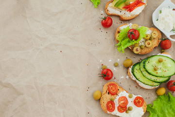 vegetarian sandwiches of toasted bread, cottage cheese, cucumbers, tomatoes, olives, lettuce leaves and green peas lie on the crumpled craft paper on the side, leaving an empty space for the inscripti