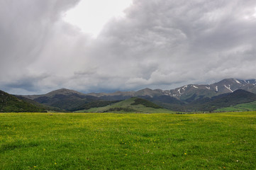 Fototapeta premium Green glade and mountains in the background. Mountains in the clouds