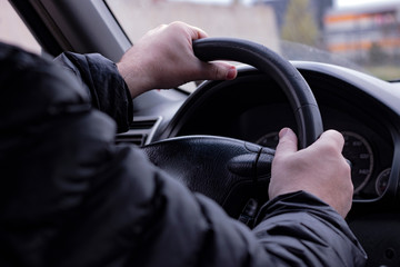 Man black jacket on driver place with steering wheel in hands.