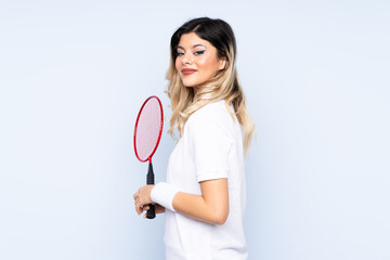 Teenager girl playing badminton isolated on blue background laughing
