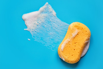 Yellow washing sponge in soap foam on a blue background isolated - obrazy, fototapety, plakaty