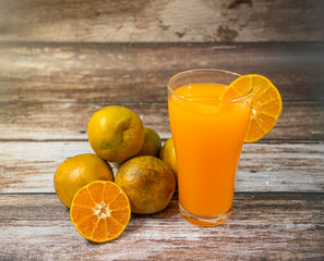 Glass of orange juice and oranges on wooden background. Orange juice on table close-up