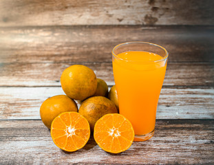 Glass of orange juice and oranges on wooden background. Orange juice on table close-up