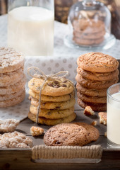 Homemade oatmeal and chocolate chip cookies in rustic wooden tray, glass of milk, bottle and polka dot towel background
