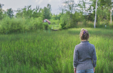 Naklejka na ściany i meble A woman stands in the background of an overgrown pond looks at a small house in the distance