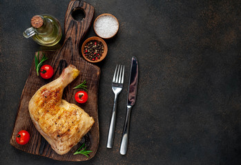 one grilled chicken leg with spices on a cutting board on a stone background
