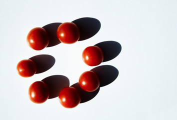 Seven small red tomatoes are on table. Tomatoes lie in the shape of circle. A long, hard shadow falls from tomatoes. A variety of vegetables-cherry tomato. There is an empty space for text in frame.