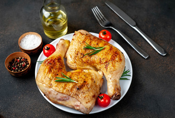 two grilled chicken legs with spices on a white plate on a stone background