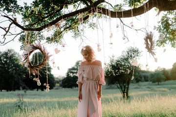 Beautiful young girl in dress with a gypsophila wreath, green grass, beautiful sunset, boho decor,...