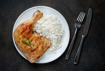 grilled chicken leg with spices and rice on a white plate on a stone background