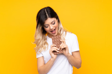 Teenager girl isolated on  yellow background eating a chocolate tablet