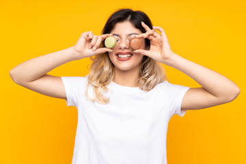 Teenager girl isolated on yellow background wearing colorful French macarons as glasses