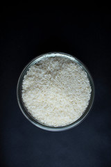White raw Rice, in a glass bowl, isolated, top view, Black Background. 