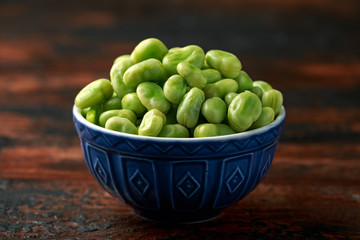 Green Broad Beans in a blue bowl on wooden table. healthy food