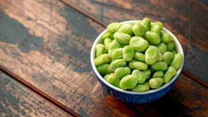 Green Broad Beans in a blue bowl on wooden table. healthy food