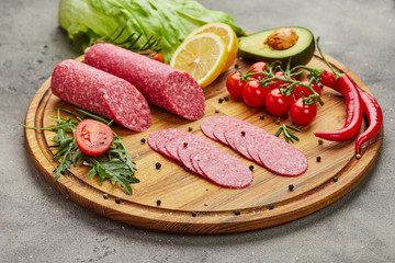 Traditional thinly sliced salami on a wooden cuttingboard  with spices, lettuce, avocado and tomatoes. Cold meat plate