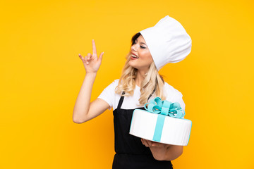 Teenager girl pastry holding a big cake isolated on yellow background pointing with the index finger a great idea