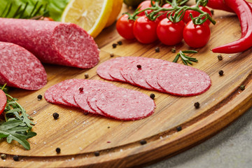 Traditional thinly sliced salami on a wooden cuttingboard  with spices, lettuce, avocado and tomatoes. Cold meat plate