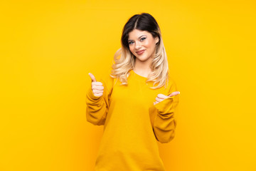 Teenager girl isolated on yellow background with thumbs up gesture and smiling