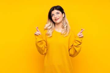 Teenager girl isolated on yellow background with fingers crossing