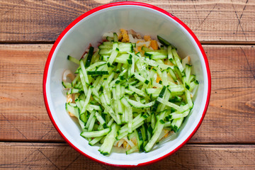 Step by step cooking of salad with squid, eggs and fresh cucumbers and herbs, step 3 - adding chopped fresh cucumbers, top view, selective focus
