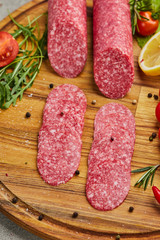 Traditional thinly sliced salami on a wooden cuttingboard  with spices, lettuce, avocado and tomatoes. Cold meat plate