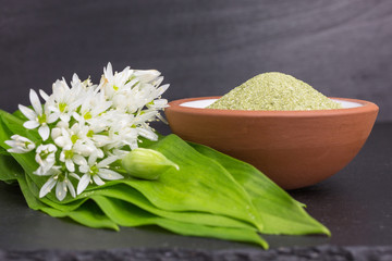 bowl of dried wild garlic salt on slate plate with leaves and blossoms, focus on the left side of the salt heap