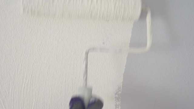 Painter Painting a House Wall with a White Paint Roller.