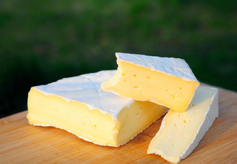 the soft texture of brie cheese is visible when cut. Triangular pieces, one bitten. Lying on a wooden board