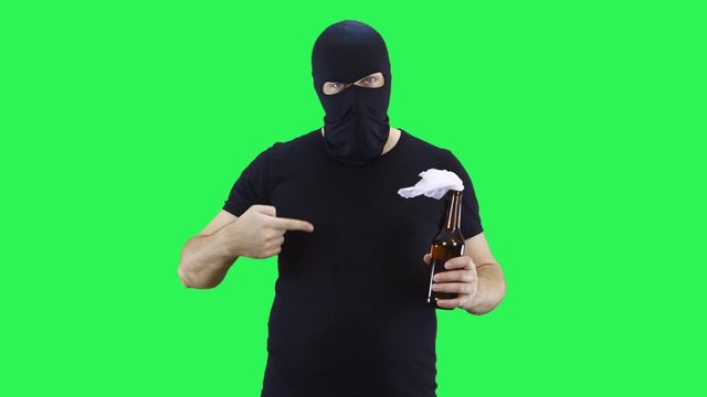 A man in a black mask holds in his hand a bottle of Molotov cocktail and points a finger at it.Balaclava.Green screen background.