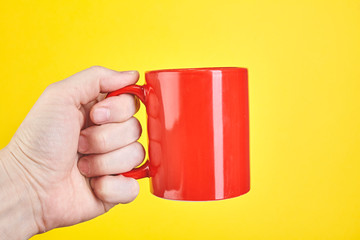 Obraz premium Male hand is holding a red cup isolated on a yellow background
