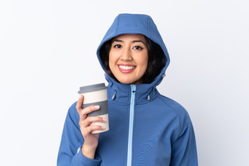 Mixed race woman wearing winter clothes with the hood on and holding a hot takeaway coffee over isolated white background smiling a lot